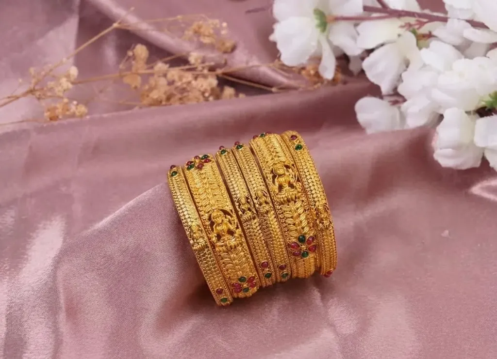 Ethereal gold-toned bangles, delicately sculpted with divine Lakshmi motifs, twirling floral vines and shimmering ruby-emerald gems, exuding regal elegance for timeless grandeur. (2.4)