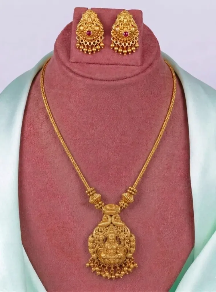 Regal gold-toned jewellery ensemble featuring an exquisite Lakshmi pendent necklace with dangling beads and matching deity earrings.