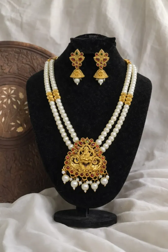 Unmissable glam two-line pearl short haram with an intricate gold Lakshmi pendant & ruby accent plus matching jhumka earrings-the ultimate festive must have that'll make you the center of attention.