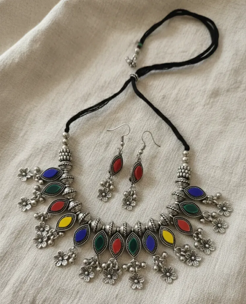 Vibrant oxidized necklace with a black cord, featuring teardrop stones in purple,green,red,blue &yellow, accented with silver floral charm, paired with matching earrings.