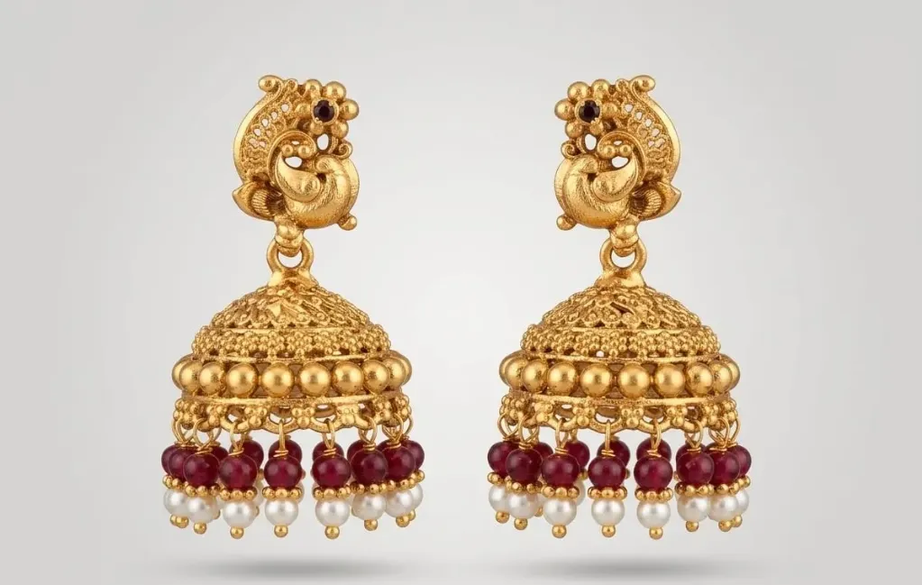 Handcrafted temple jhumka earrings featuring gold-plated peacock motifs with black gemstones, intricate dome design, and layered beads of ruby-red stones topped with pearls for an elegant traditional look.