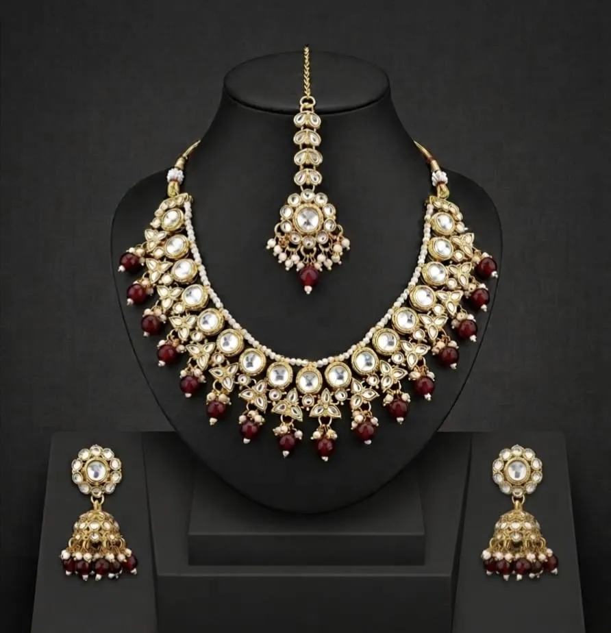 An exquisite kundan-polki jewelry set. Handcrafted in gold with radiant white stones and deep red gemstone accents. Featuring a statement necklace, matching earrings, and a maang tikka, this ensemble elegance-perfect for wedding and grand occasions.