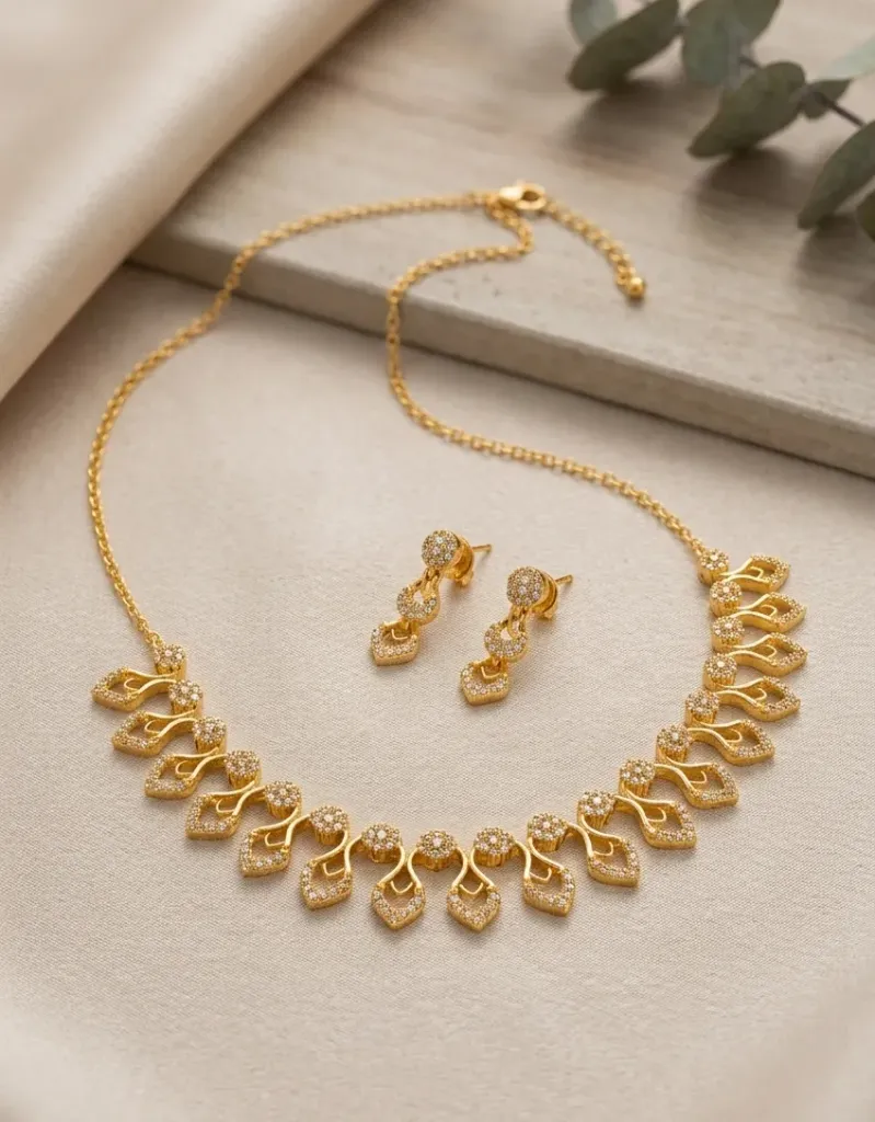 A dazzling gold-toned necklace adored with elegant swirl charms and shimmering diamond-kissed accents, paired with matching earrings that catch every glance and add regal sparkle to any attire, making you feel like royalty in every moment.