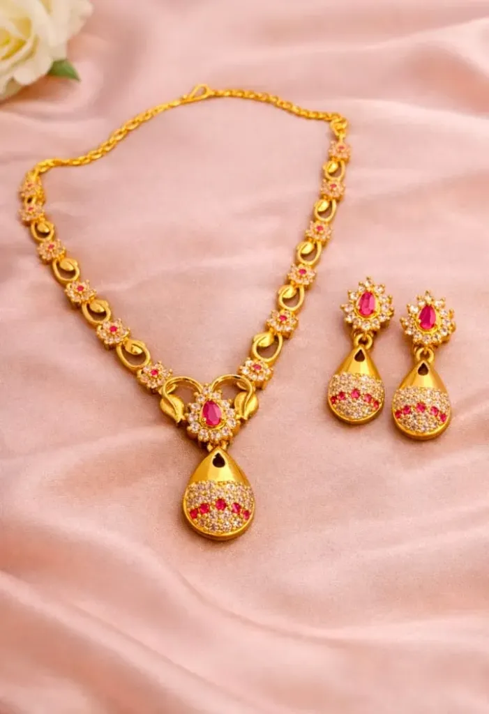 Elegant gold-toned necklace and earring set embellished with pink ruby-like stones and sparkling white zirconia, crafted in a classical teardrop design for luxurious look.