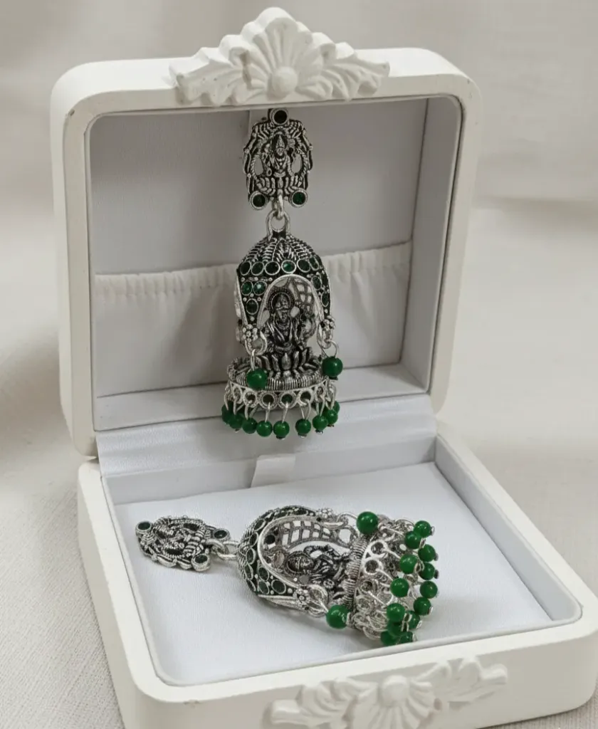Exquisite oxidized Temple Jhumkas featuring a detailed Goddess Lakshmi motif and vibrant emerald-green bead accents.