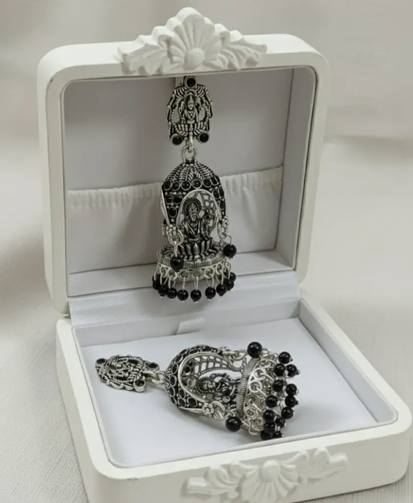 Exquisite oxidized silver Jhumkas featuring intricate temple-inspired motifs and delicate black bead droplets for a timeless ethnic look.
