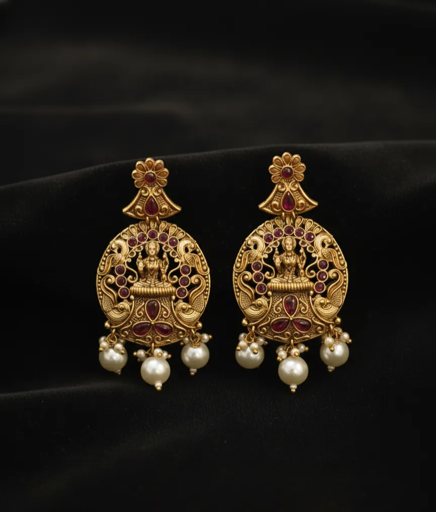 Exquisite Temple Jewellery earrings featuring a divine Goddess Lakshmi motif, intricately crafted in antique gold finish with ruby-red stones and elegant pearl drops.