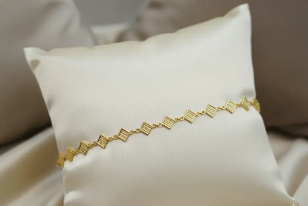 This delicate gold-toned bracelet features a refined chain of textured diamond-shaped motifs, offering a graceful balance of modern style and classic charm.