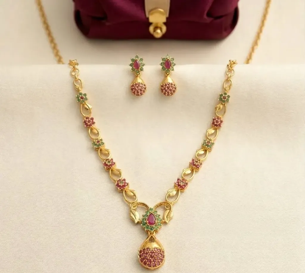 Elevate Your Festive ensemble with this exquisitely crafted gold toned necklace set, featuring intricated floral motifs adorned with vibrant ruby and emerald-colored stones.