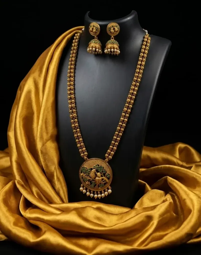 Gold toned necklace & jhumka earring with an exquisite peacock-embossed pendent and pearl detailing-perfect for making a timeless traditional statement.