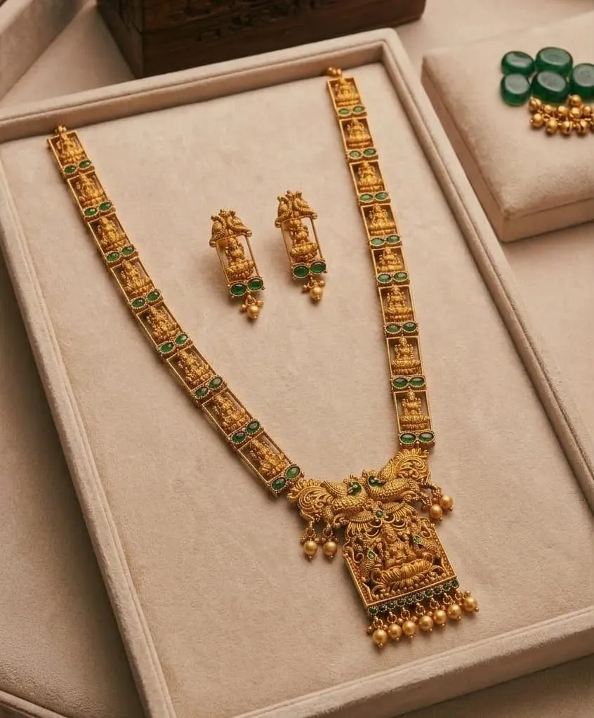 Traditional gold toned necklace set with green gemstones, featuring intricate cravings and divine motifs.