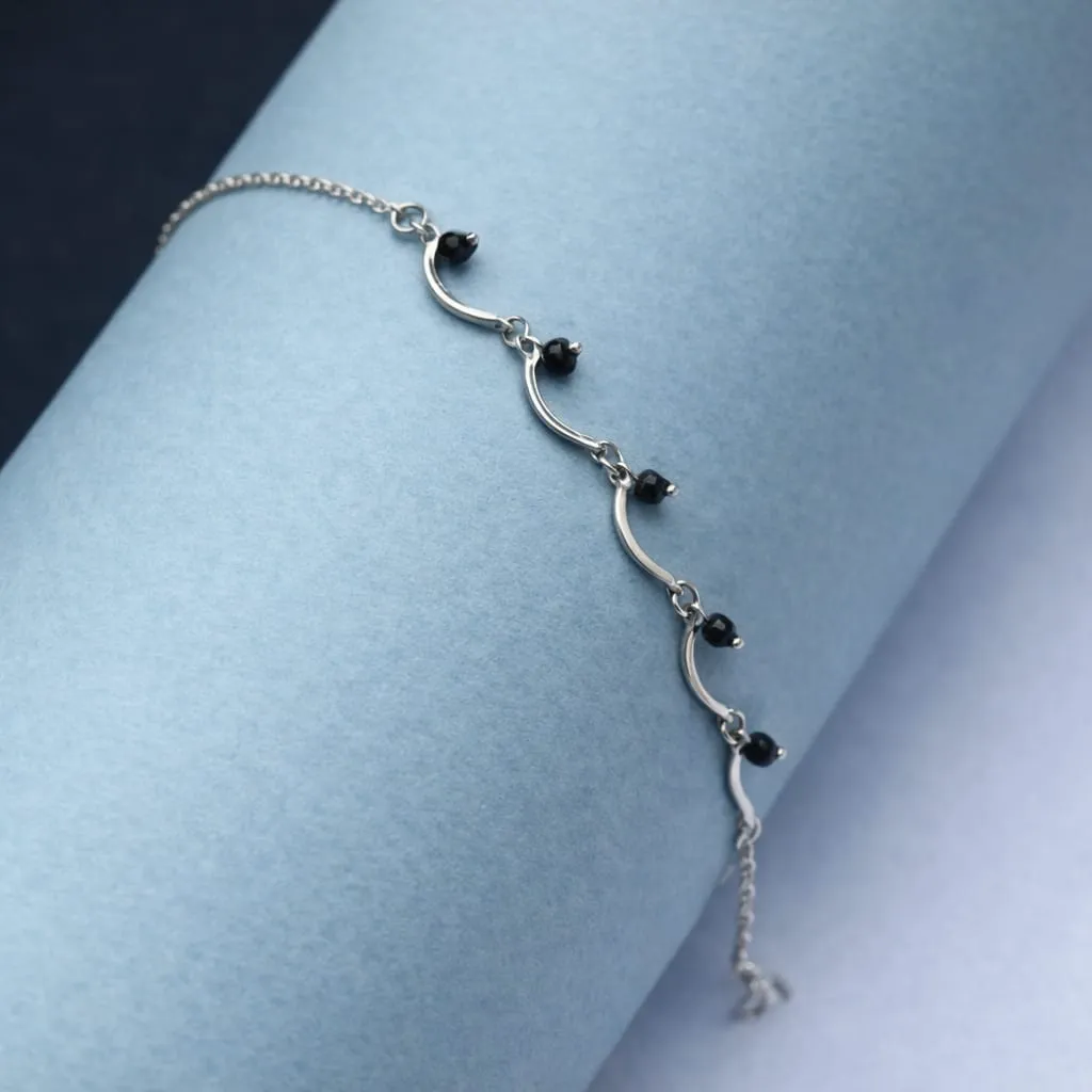 A sleek silver bracelet with wavy bar links and tiny black beads.